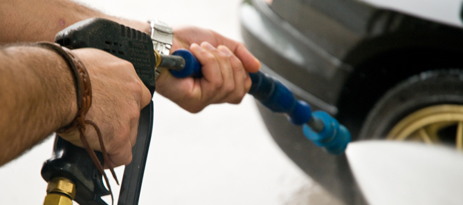 Hands using high-powered pressure washer at self-service car wash bay